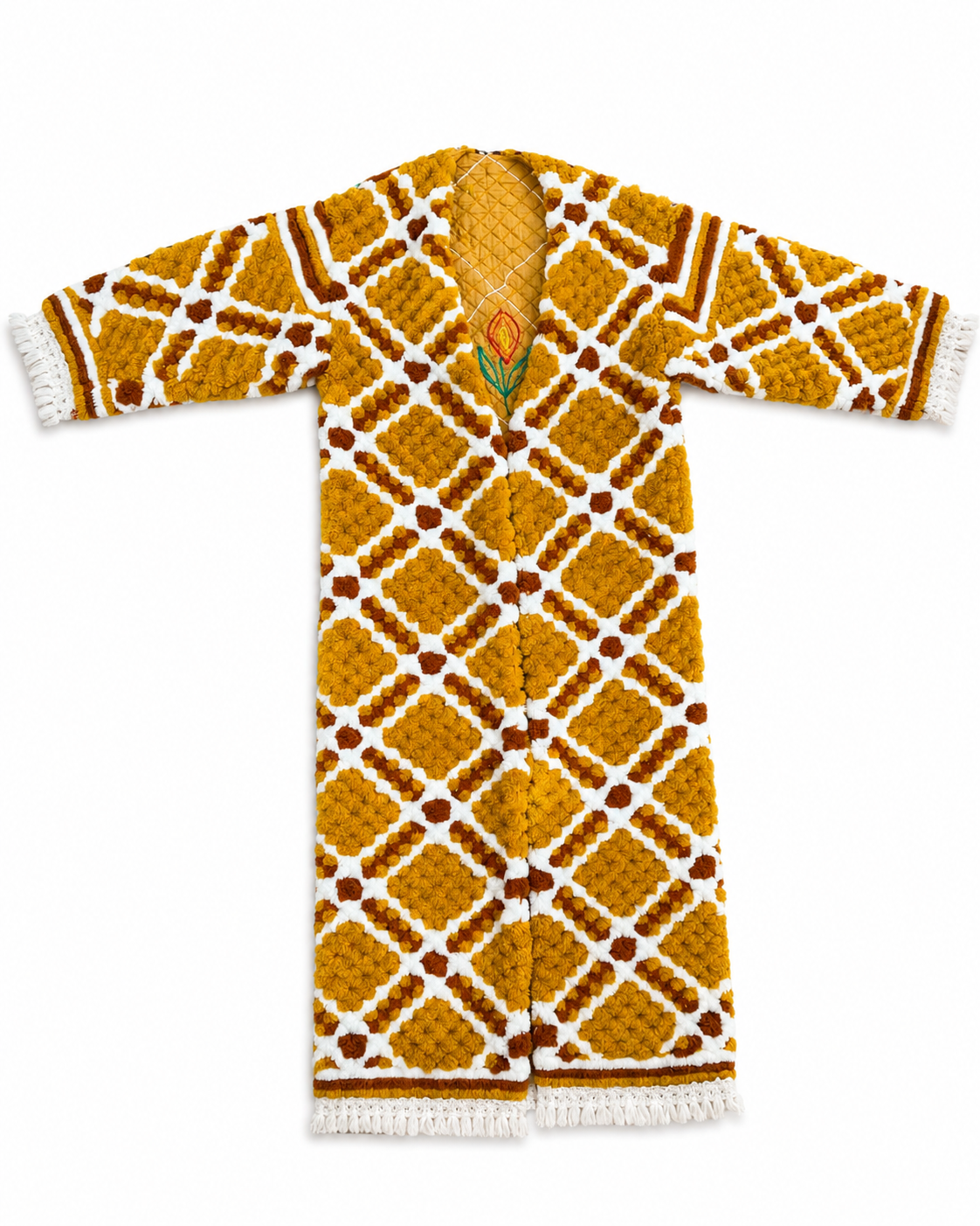 A long-sleeve open-front cardigan with a textured geometric pattern in mustard yellow, white, and brown, featuring a small embroidered floral detail at the neckline and white tassel fringe on the cuffs and hem.